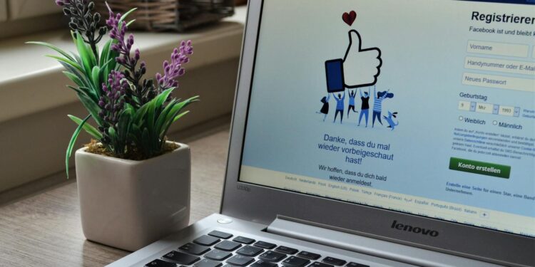 A Lenovo laptop displaying Facebook login beside a lavender plant indoors.